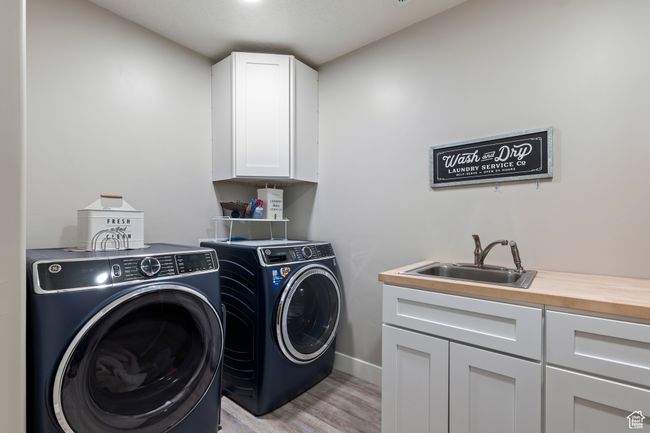Clothes washing area with washing machine and clothes dryer, light wood-style flooring, a sink, baseboards, and cabinet space | Image 28