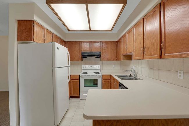 Kitchen featuring white appliances, under cabinet range hood, light countertops, tasteful backsplash, and brown cabinetry | Image 14