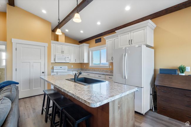 Kitchen with white appliances, light wood-style flooring, vaulted ceiling with beams, and a sink | Image 10