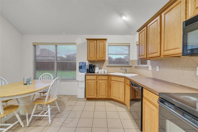 Kitchen featuring black appliances, lofted ceiling, decorative backsplash, light tile patterned floors, and light countertops | Image 11