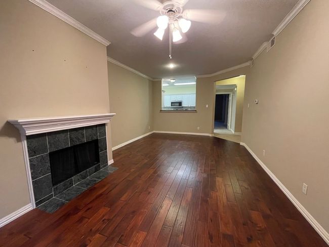 Unfurnished living room with a ceiling fan, a fireplace, dark wood-style flooring, and ornamental molding | Image 6