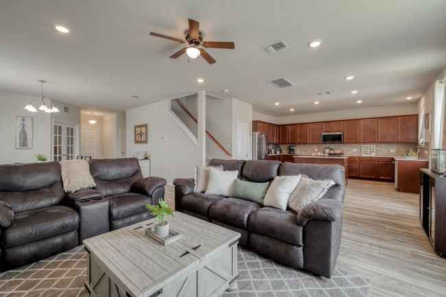 Living room with ceiling fan with notable chandelier, stairway, light wood finished floors, and visible vents | Image 11