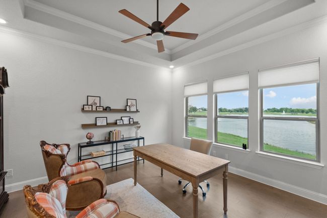 Dedicated office space with a tray ceiling, wood floors, water views, a ceiling fan, and crown molding | Image 23