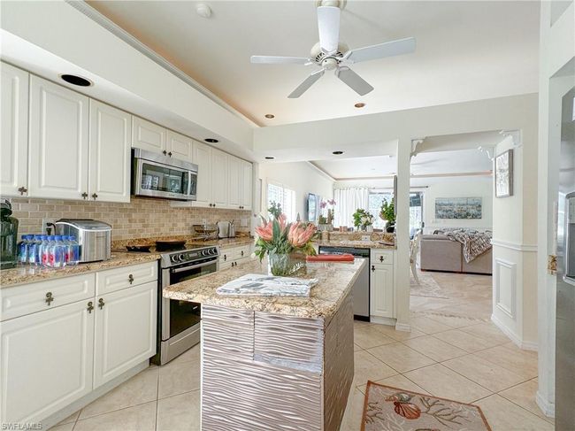 Kitchen with stainless steel appliances, backsplash, white cabinetry, a center island, and light stone countertops | Image 38
