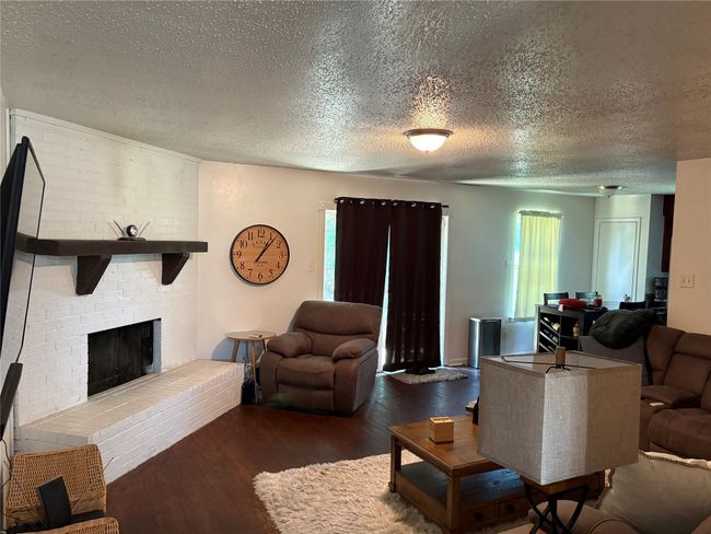 Living area with wood finished floors, a textured ceiling, and a brick fireplace | Image 6