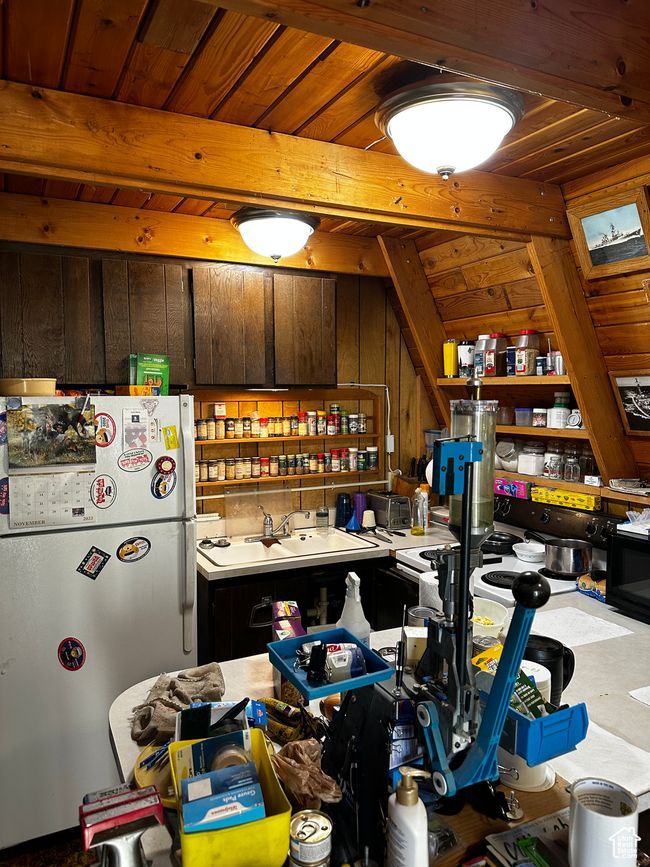 Kitchen featuring wooden walls, freestanding refrigerator, a sink, light countertops, and beam ceiling | Image 5