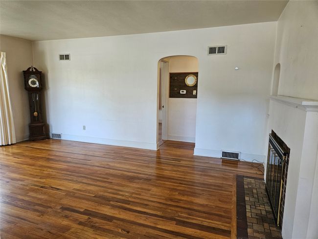 Unfurnished living room with visible vents, arched walkways, wood finished floors, and a fireplace | Image 6