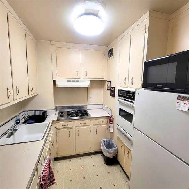 Kitchen with white oven, stainless steel gas cooktop, a sink, under cabinet range hood, and light countertops | Image 6