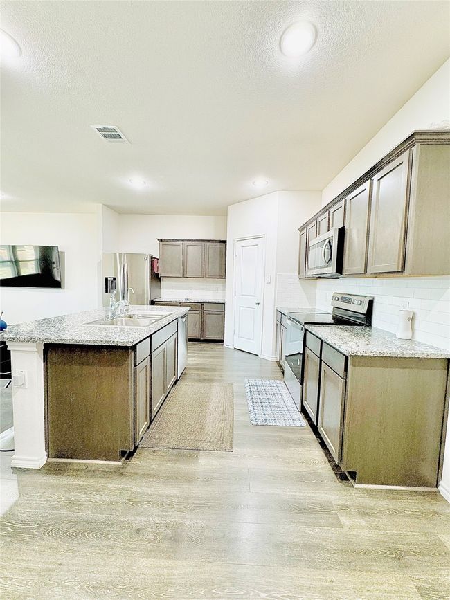 Kitchen with appliances with stainless steel finishes, light wood-style floors, a sink, an island with sink, and backsplash | Image 9