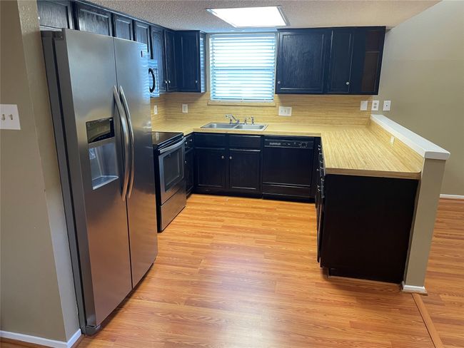 Kitchen featuring stainless steel appliances, tasteful backsplash, a textured ceiling, light hardwood / wood-style flooring, and sink | Image 5