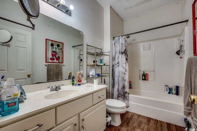 Full bathroom with toilet, vanity, wood finished floors, shower / tub combo with curtain, and a textured ceiling | Image 21