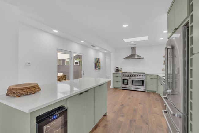 Kitchen featuring beverage cooler, recessed lighting, wall chimney exhaust hood, green cabinets, and premium appliances | Image 21