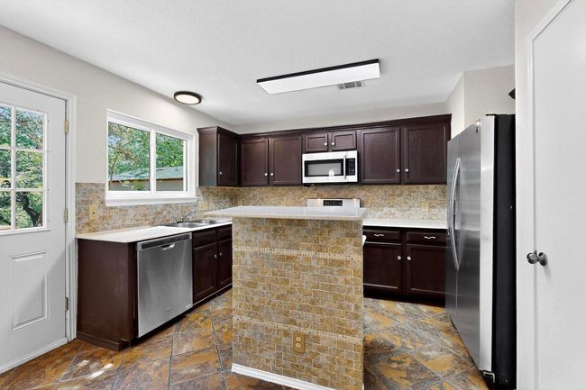 Kitchen with appliances with stainless steel finishes, dark brown cabinets, tasteful backsplash, and dark stone finish floors | Image 12