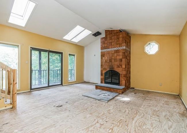 Unfurnished living room featuring a fireplace and lofted ceiling with skylight | Image 14