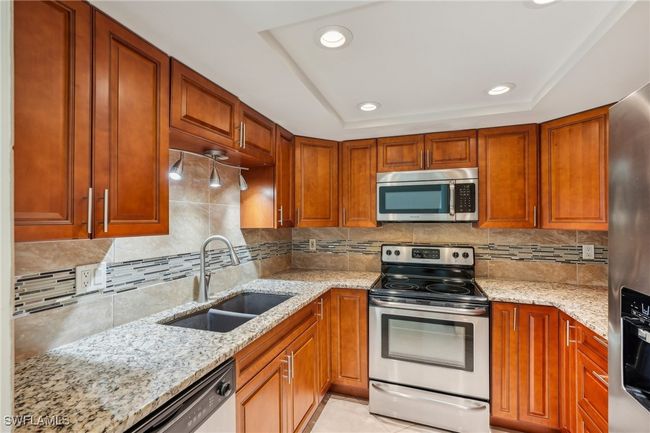 Kitchen featuring appliances with stainless steel finishes, light stone counters, a tray ceiling, recessed lighting, and brown cabinets | Image 13