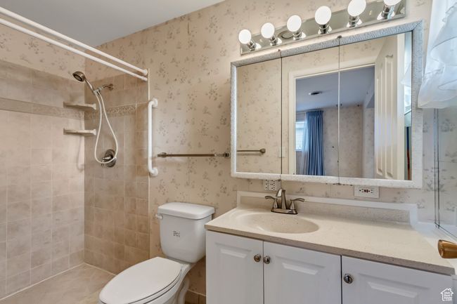 Full bath featuring wallpapered walls, toilet, vanity, and tiled shower | Image 13