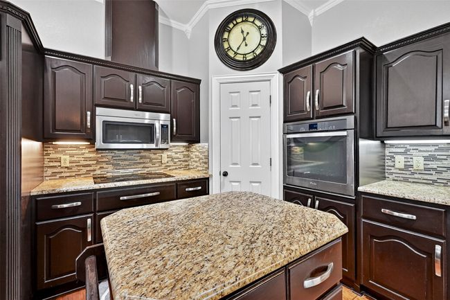 Kitchen with stainless steel appliances, crown molding, light stone counters, dark brown cabinets, and tasteful backsplash | Image 15