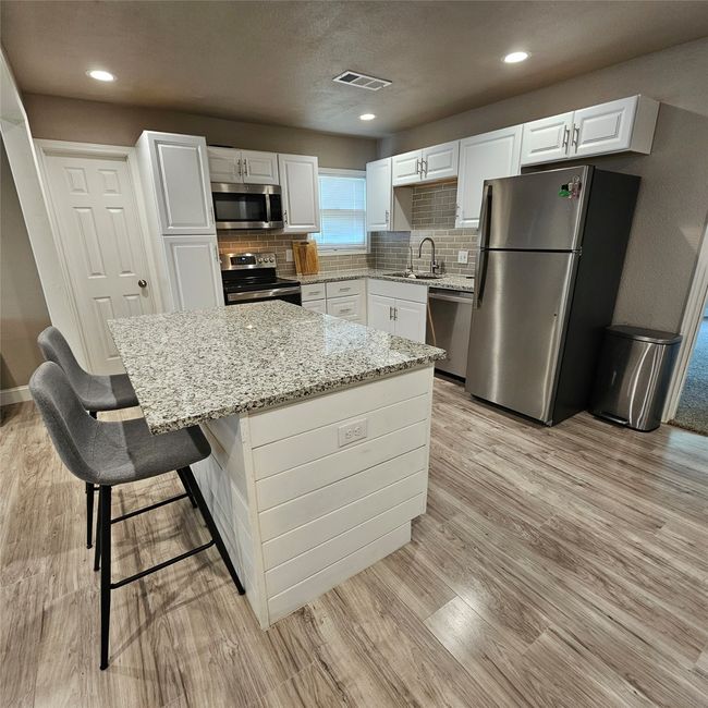 Kitchen with appliances with stainless steel finishes, a sink, light stone countertops, light wood-type flooring, and recessed lighting | Image 11