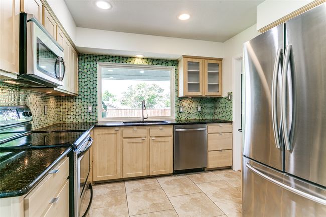 Kitchen featuring appliances with stainless steel finishes, light brown cabinetry, tasteful backsplash, glass insert cabinets, and granite countertops. | Image 9
