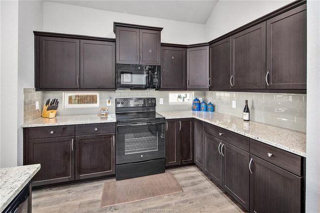 Kitchen featuring black appliances, light hardwood / wood-style floors, backsplash, and vaulted ceiling | Image 8
