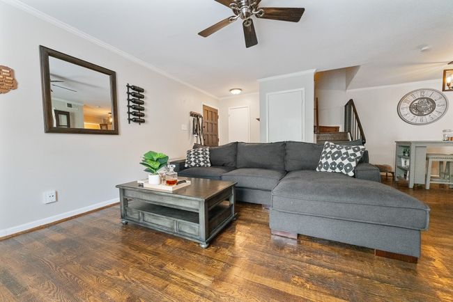 Living area with ornamental molding, wood finished floors, stairway, a ceiling fan, and baseboards | Image 4