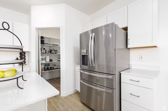 Kitchen featuring white cabinetry, light countertops, light wood finished floors, and stainless steel fridge with ice dispenser | Image 15
