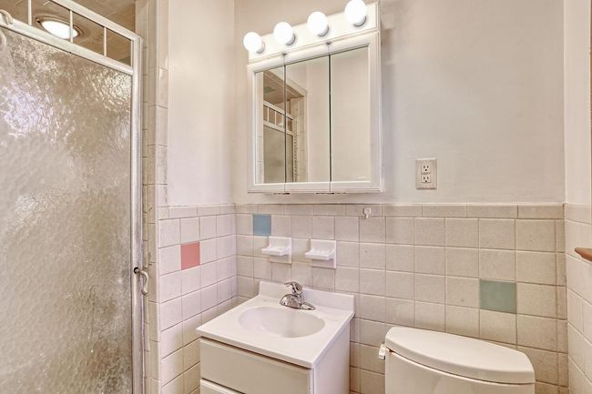 Full bathroom with toilet, wainscoting, tile walls, a stall shower, and vanity | Image 17