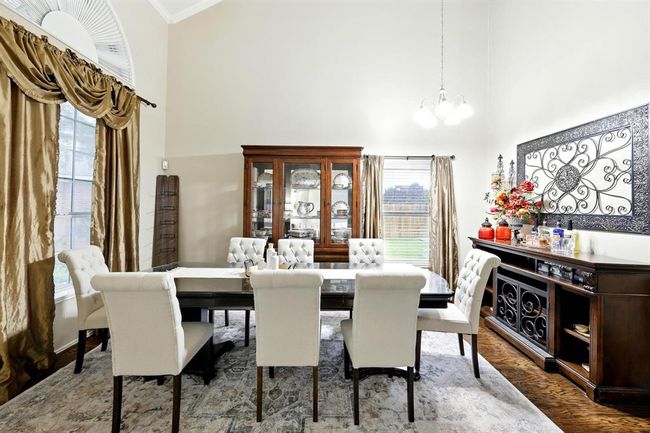 Light-filled dining room features tall windows, chandelier, and space for a large dining set, ideal for entertaining. | Image 4