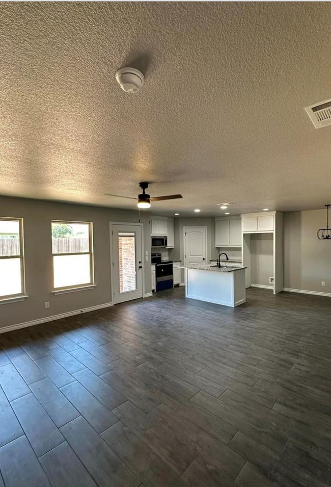 Unfurnished living room with a textured ceiling, dark wood-style floors, and ceiling fan | Image 6