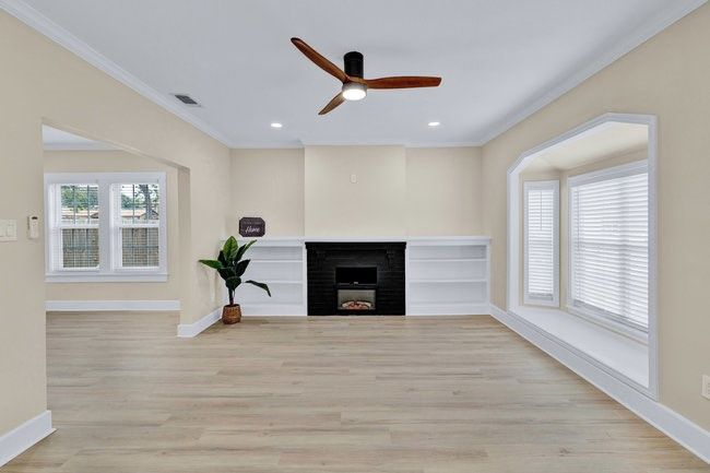Unfurnished living room featuring light wood-style flooring, a fireplace, baseboards, a ceiling fan, and crown molding | Image 4