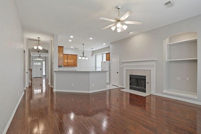 Unfurnished living room with a ceiling fan, a tile fireplace, dark wood-style flooring, a chandelier, and recessed lighting | Image 7