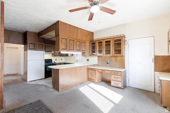 Kitchen with light countertops, black range with electric stovetop, freestanding refrigerator, a peninsula, and glass insert cabinets | Image 21