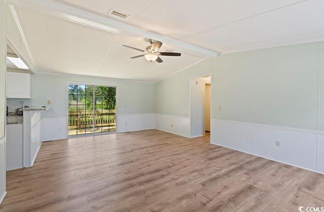 Unfurnished living room featuring a ceiling fan, light wood-type flooring, wainscoting, and a decorative wall | Image 7