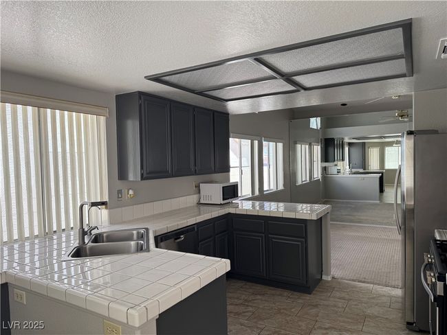 Kitchen featuring white microwave, a peninsula, dishwashing machine, plenty of natural light, and a textured ceiling | Image 4