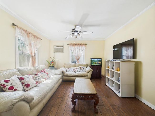 Living area with a ceiling fan, ornamental molding, plenty of natural light, dark wood-style floors, and a wall mounted AC | Image 5