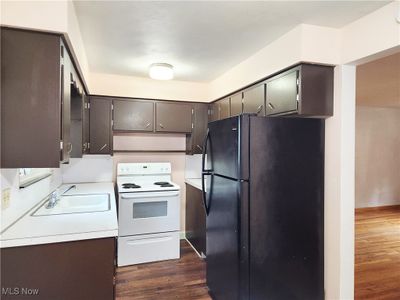 Kitchen featuring dark wood-type flooring, black refrigerator, sink, dark brown cabinetry, and white electric range oven | Image 2