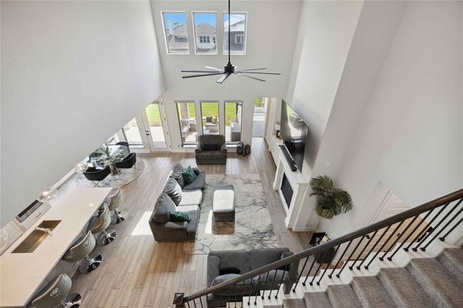 This spacious living area features a high ceiling with large windows, flooding the room with natural light. It includes an open-plan layout with a modern kitchen, cozy seating area, and a stylish fireplace, offering a perfect blend of comfort and elegance. | Image 27