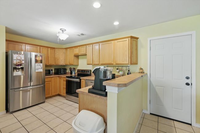 Kitchen featuring light tile patterned floors, a peninsula, light countertops, visible vents, and appliances with stainless steel finishes | Image 11