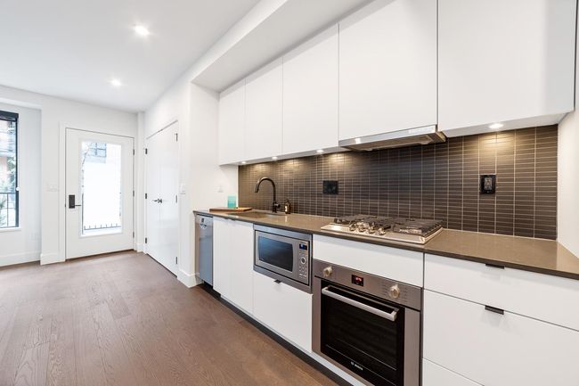Kitchen with stainless steel appliances, range hood, dark wood-style flooring, white cabinetry, and decorative backsplash | Image 22