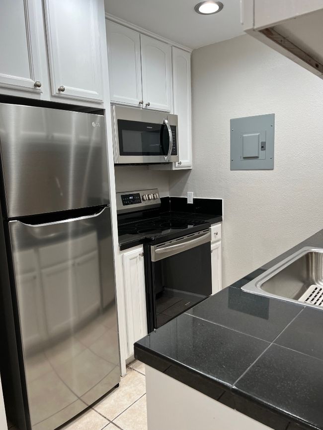 Kitchen featuring dark countertops, electric stove, electric panel, and refrigerator | Image 9