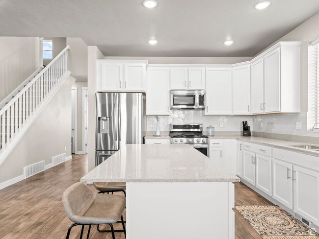 Kitchen with appliances with stainless steel finishes, a center island, a kitchen bar, backsplash, and light wood-type flooring | Image 10