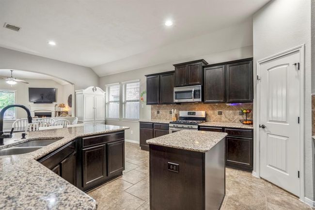 From near the fridge, take in the rich dark cabinetry paired with beautiful granite counters that offer plenty of workspace. The elegant tile backsplash and floors add texture and style, while the dual-basin undermount sink with a pull-down faucet blends function with sleek design—your kitchen ready for every tasks. | Image 9