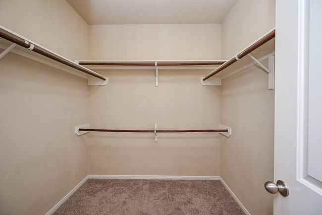 This is a spacious walk-in closet with multiple wooden shelves and hanging rods, featuring neutral walls and carpeted flooring. | Image 29
