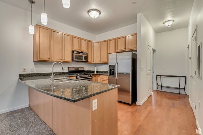 Kitchen featuring a sink, appliances with stainless steel finishes, a peninsula, decorative light fixtures, and dark stone counters | Image 10
