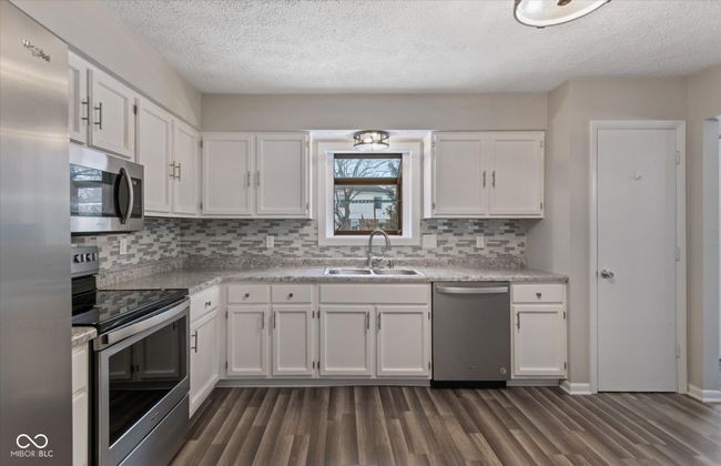 kitchen with appliances with stainless steel finishes, dark wood-style flooring, white cabinetry, decorative backsplash, and a textured ceiling | Image 5