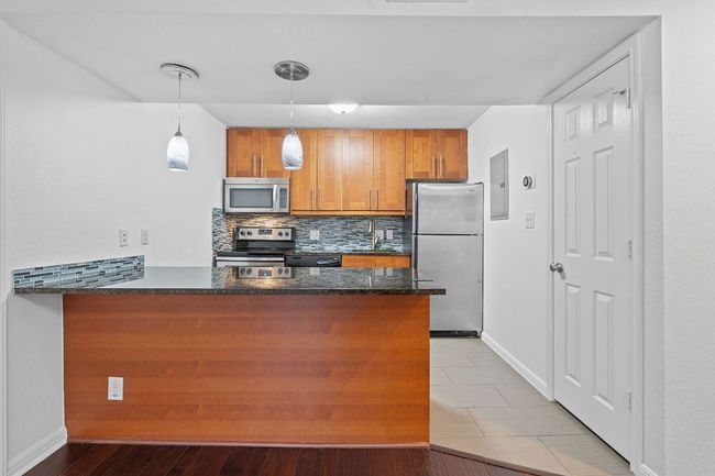 Kitchen featuring backsplash, dark stone counters, brown cabinets, a peninsula, and stainless steel appliances | Image 10