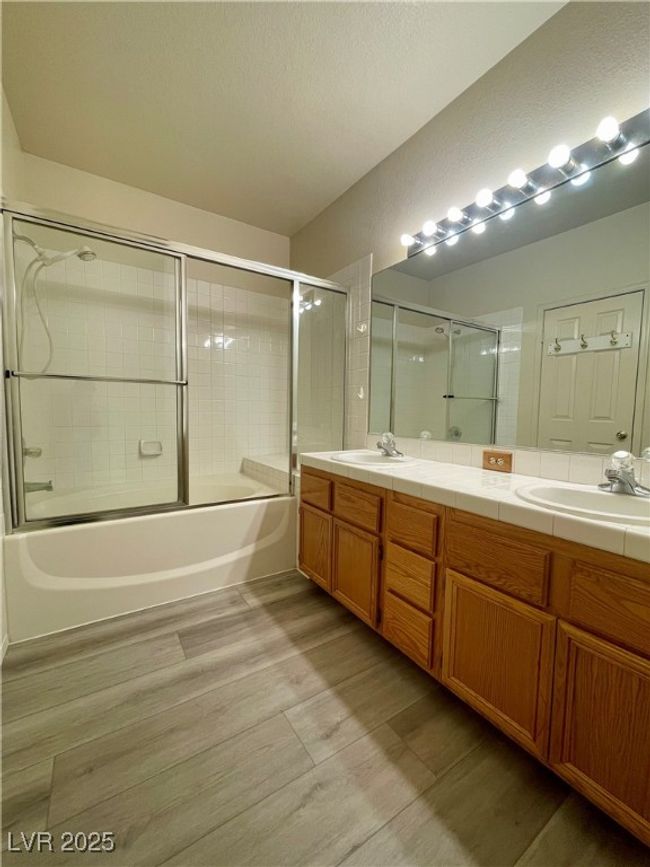 Full bath featuring double vanity, wood finished floors, bath / shower combo with glass door, and a sink | Image 7