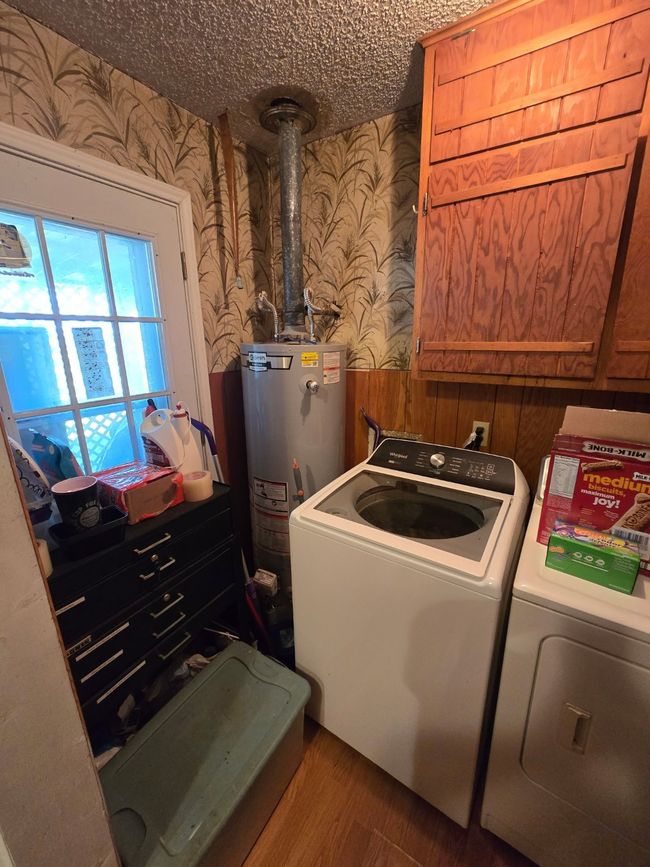 Laundry area with wallpapered walls, cabinet space, washing machine and dryer, wood finished floors, and gas water heater | Image 29