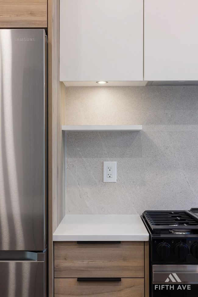 Kitchen view of freestanding refrigerator, range with gas cooktop, light countertops, and modern cabinets | Image 14