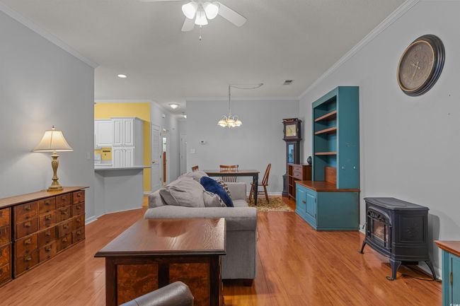 Living area featuring a wood stove, ornamental molding, ceiling fan, light wood-type flooring, and a chandelier | Image 20